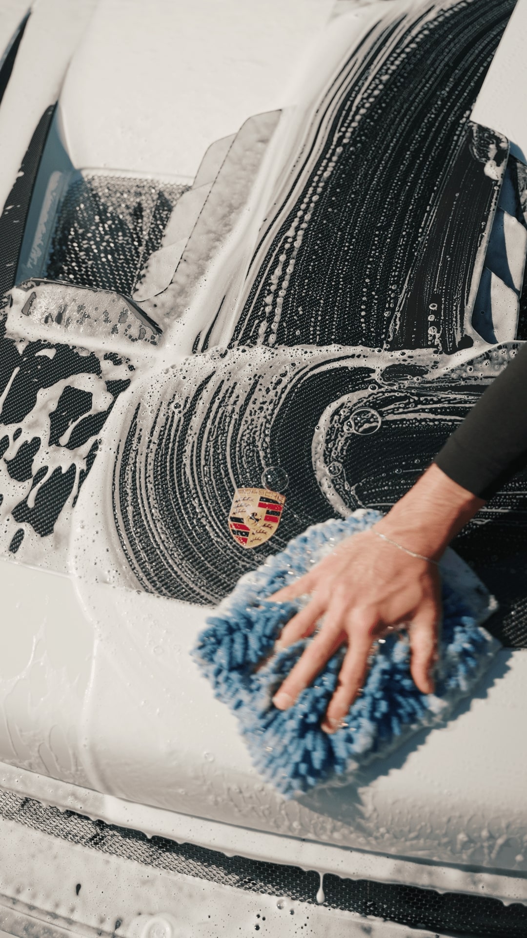 Washing a Porsche with a blue microfiber cloth, soap suds and logo visible