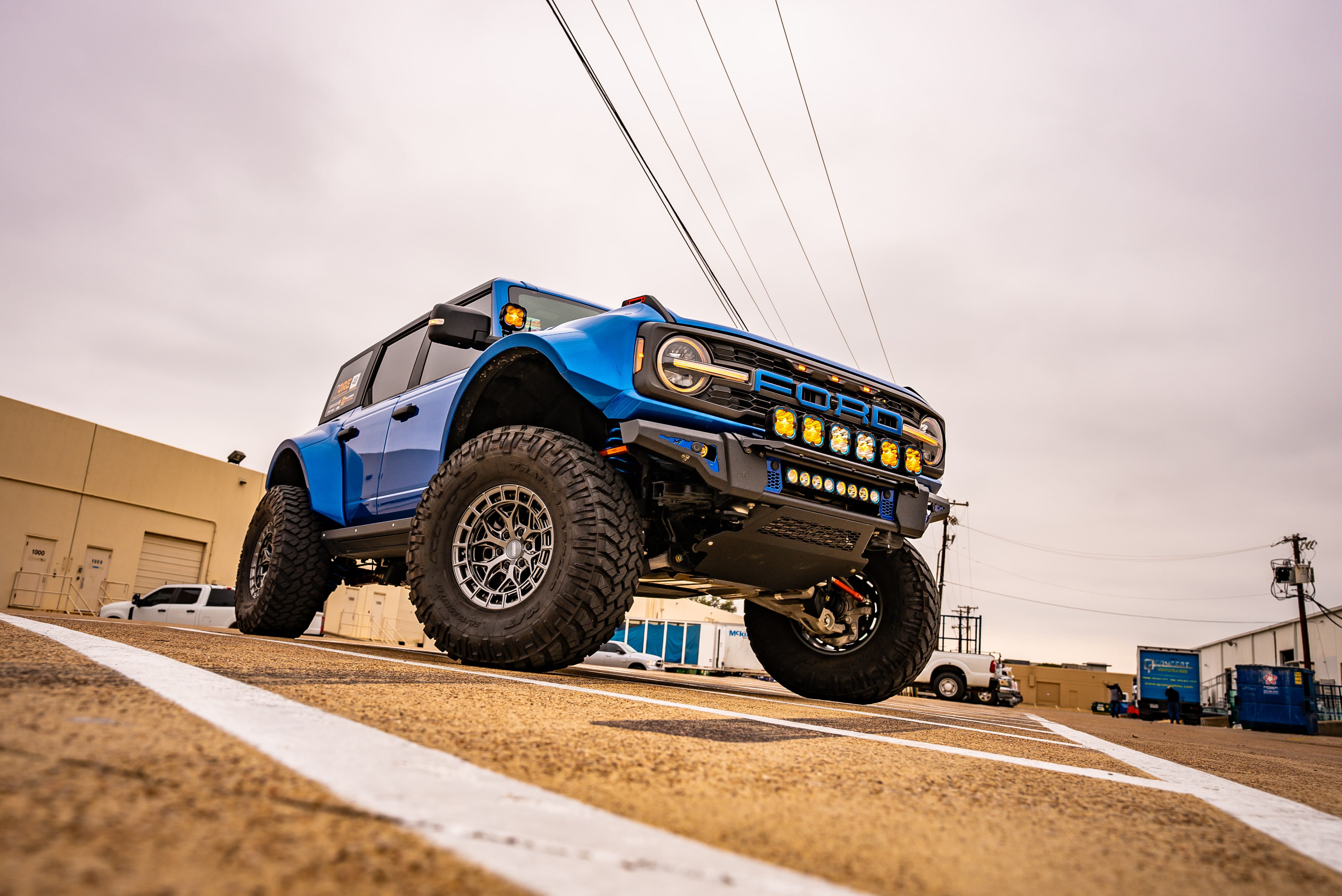 Blue Ford Bronco with massive tires and off-road lights on industrial lot