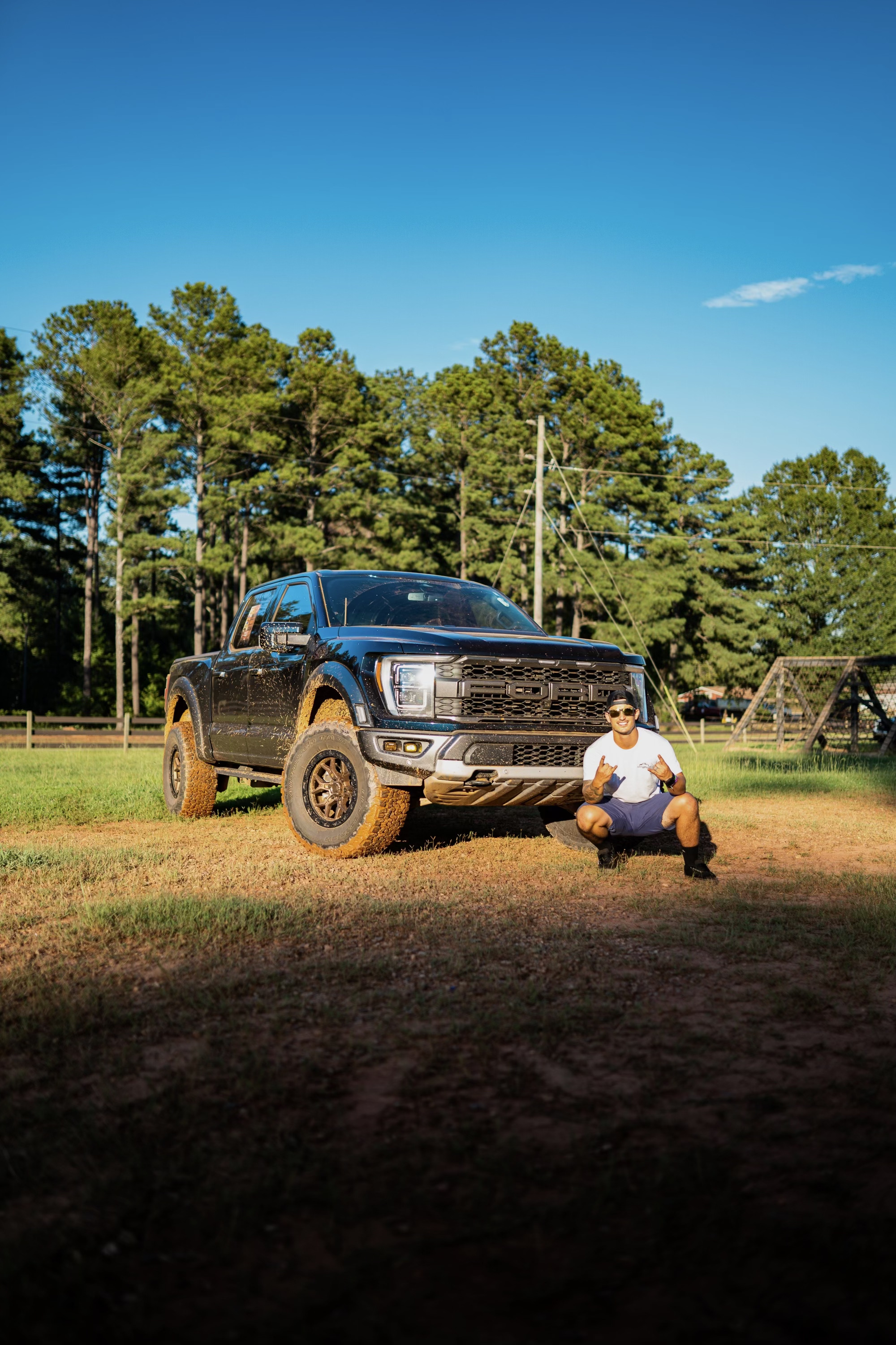 Muddy Ford Raptor truck parked in grassy field with pine trees