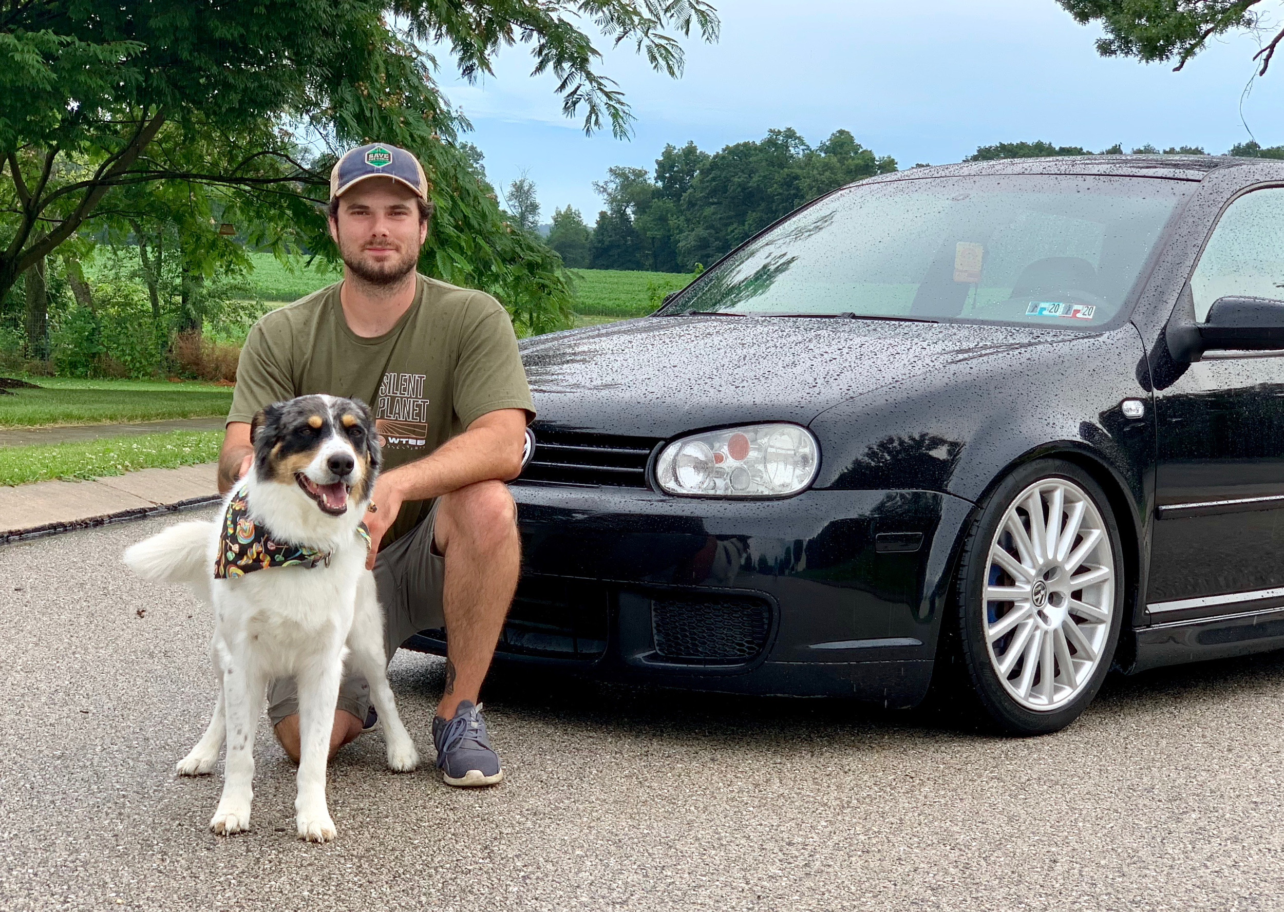 Man sitting with his friendly dog beside a black Volkswagen Golf
