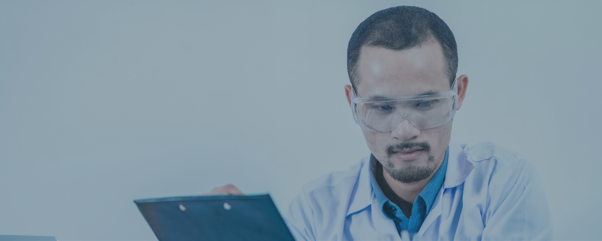 Chemiker im Labor mit Schutzbrille und Handschuhen überprüft Unterlagen neben Reagenzgläsern und Laborflaschen