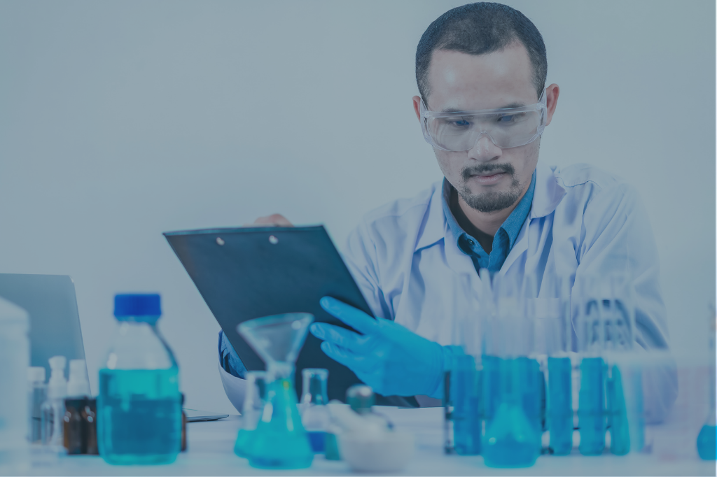 Chemist in a lab wearing safety goggles and gloves, checking documentation next to test tubes and laboratory bottles.