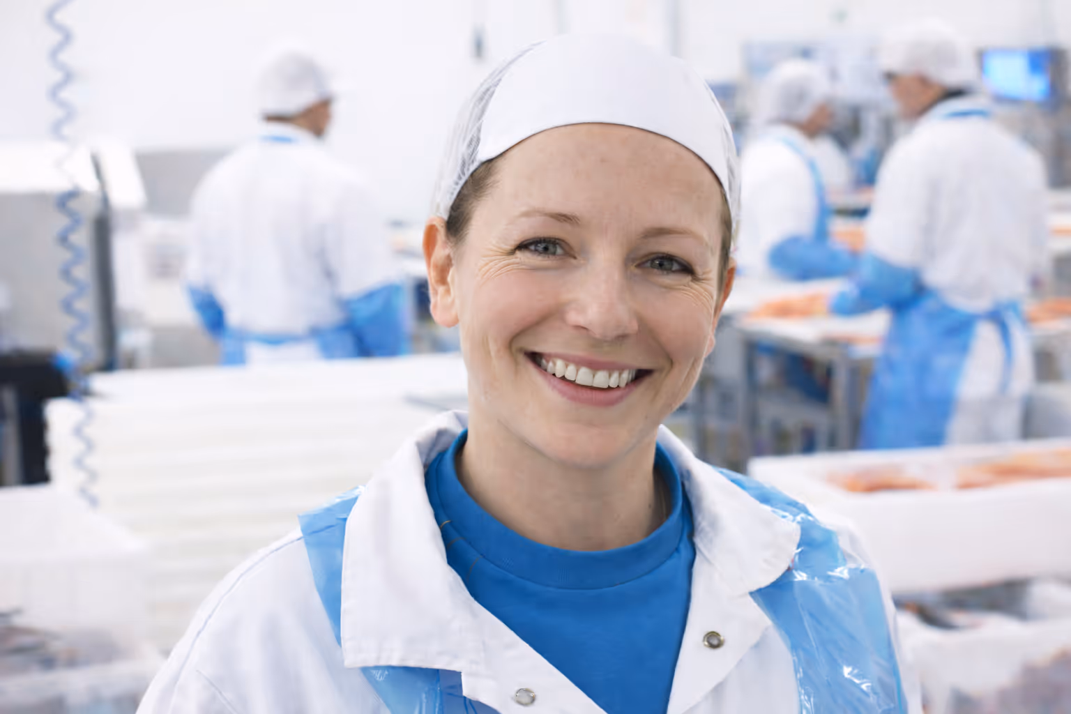 Smiling woman in protective clothing and hairnet in a food processing facility.