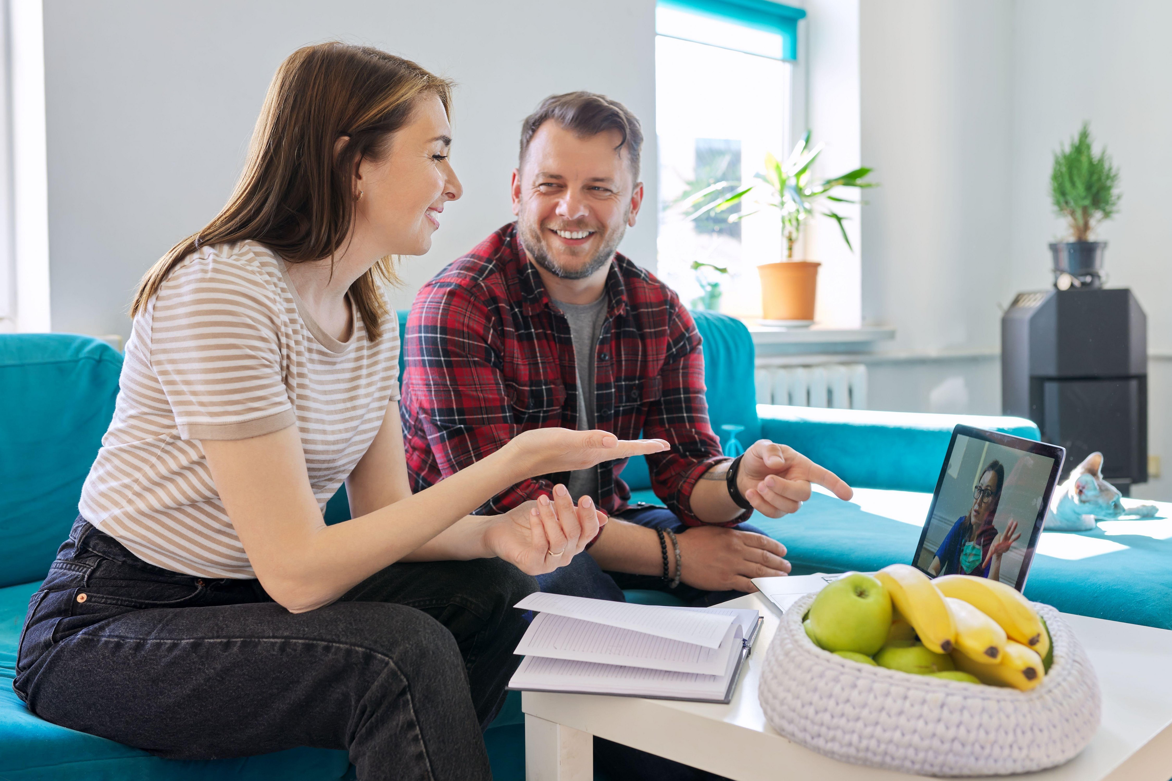 Image of woman and man looking at laptop in living room with a bowl of fruit