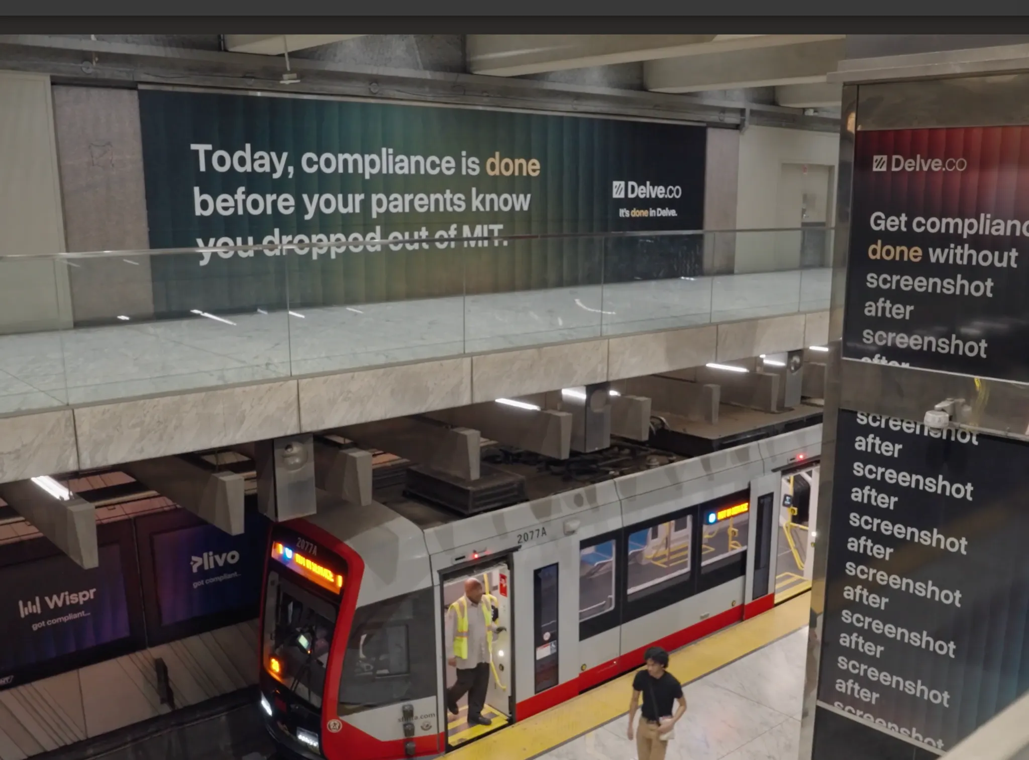 View of a train station platform with a white and red train, a person in a yellow safety vest standing at the open door, a man walking on the platform, and large advertisements on the walls featuring compliance-related slogans.