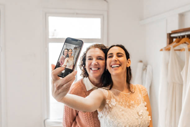 Close-up of a bride taking selfie with her mother in a bridal shop Close-up of a bride taking selfie with her mother in a bridal shop wedding photo mom and bride stock pictures, royalty-free photos & images