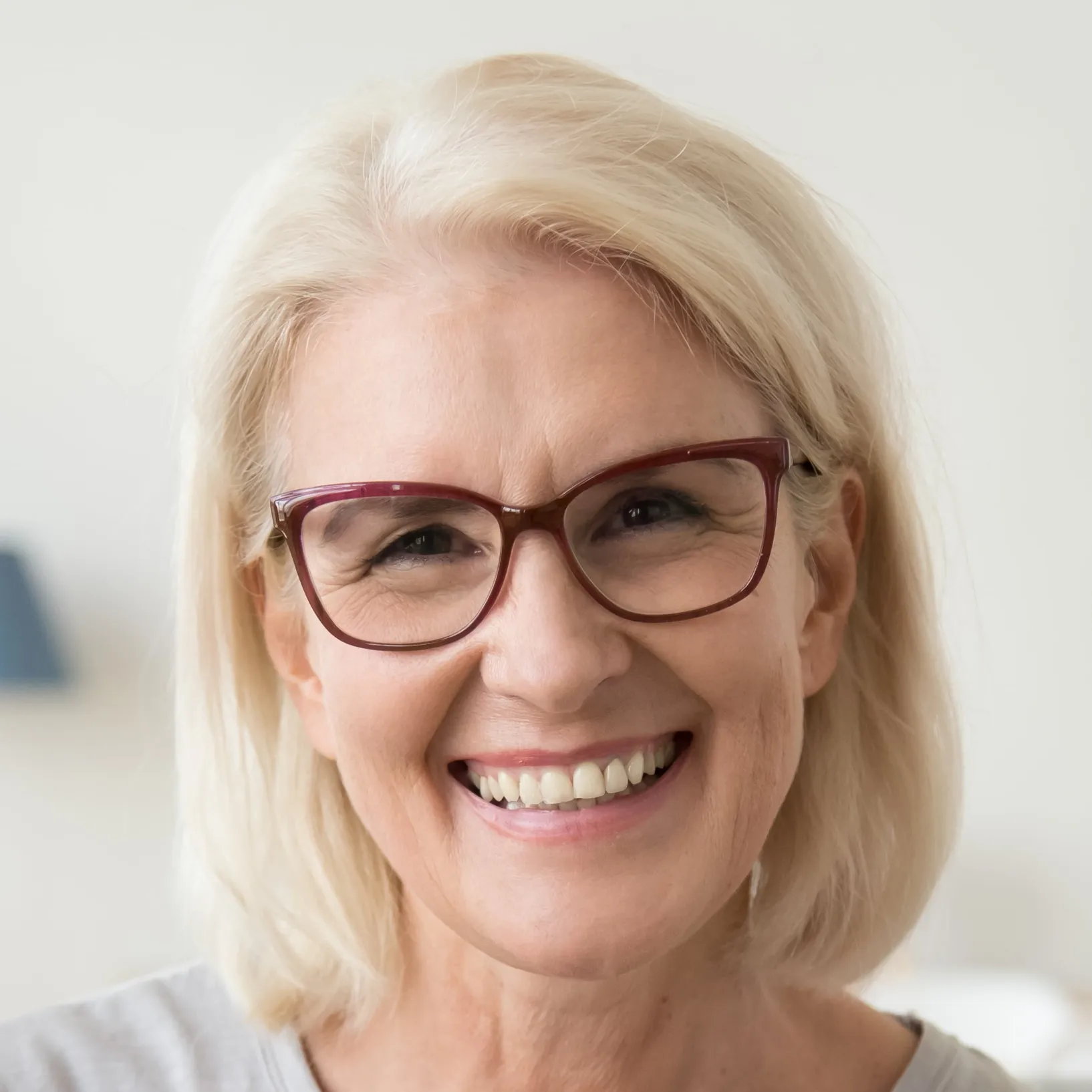 Close-up of a smiling middle-aged woman with blonde hair and red glasses.
