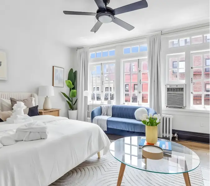 Modern two-story house with a black and white exterior, a driveway with a parked silver SUV, surrounding greenery, and a fenced garden.