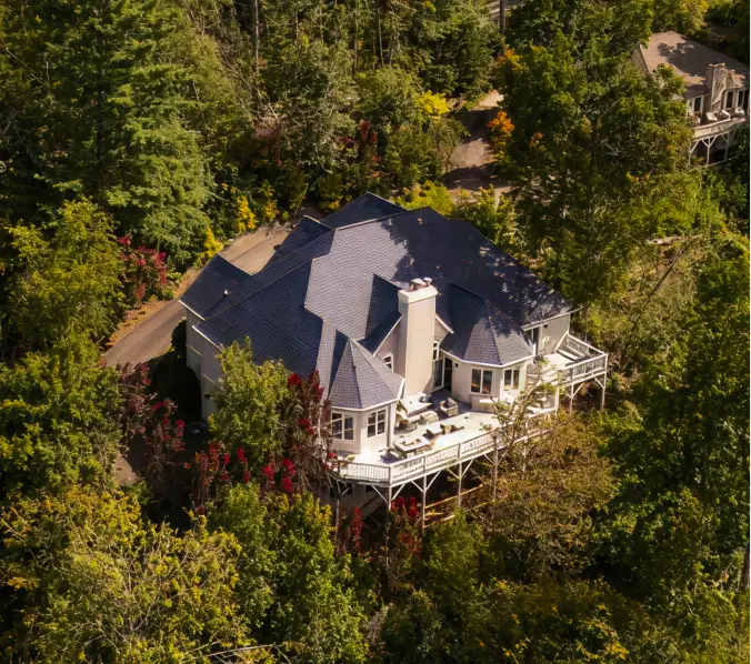 Modern two-story house with a black and white exterior, a driveway with a parked silver SUV, surrounding greenery, and a fenced garden.