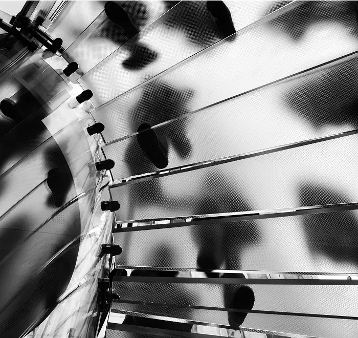 Black and white photo of people walking on a textured, translucent spiral staircase viewed from below.
