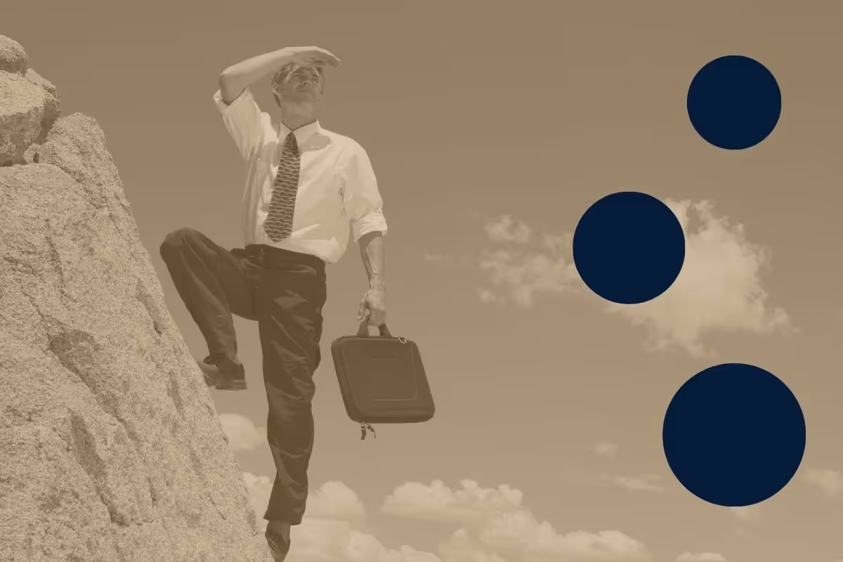 A professionally dressed man holding a briefcase while standing on the side of a mountain and looking off into the distance