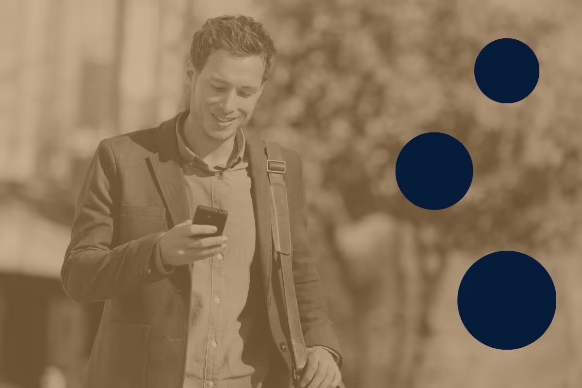 A professionally-dressed man smiling and looking down at the smartphone he is holding