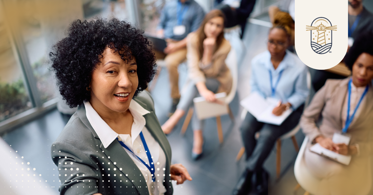 A woman speaking to a seated group taking notes in an office setting, representing the corporate teams and roles companies often overlook when hiring.