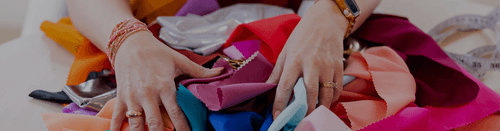 Hands sorting through colorful fabric swatches with a measuring tape nearby.