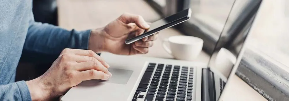 Woman sitting at her laptop browsing through her phone