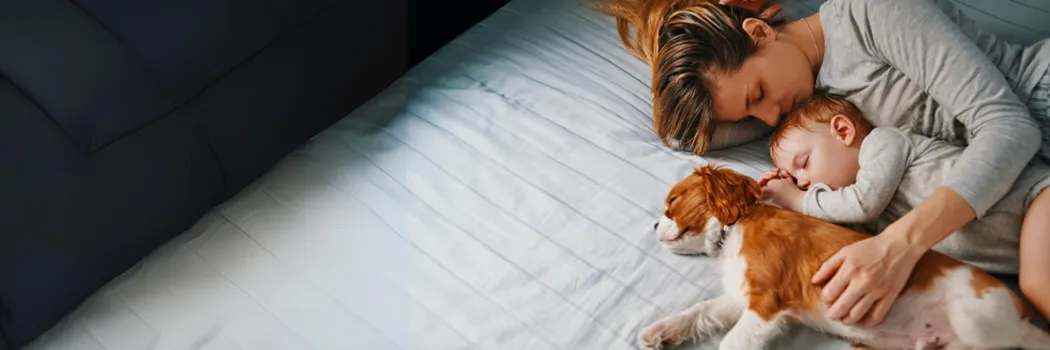 Woman and infant laying down sleep with their dog