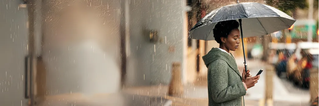 Woman standing in the rain with an umbrella while looking at her mobile phone