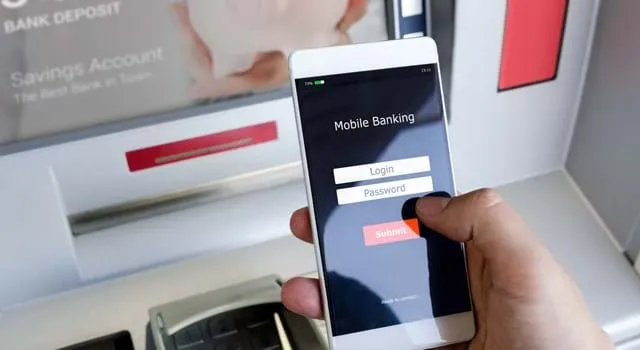 Person at an ATM looking at their mobile with a screen showing mobile banking