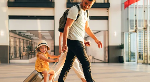 Man walking through the airport with child sitting on luggage