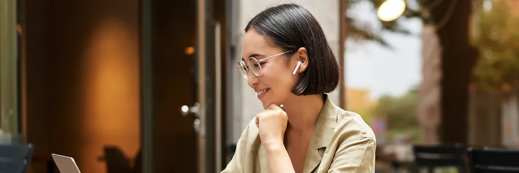 A young women with earphones on looking at her laptop screen