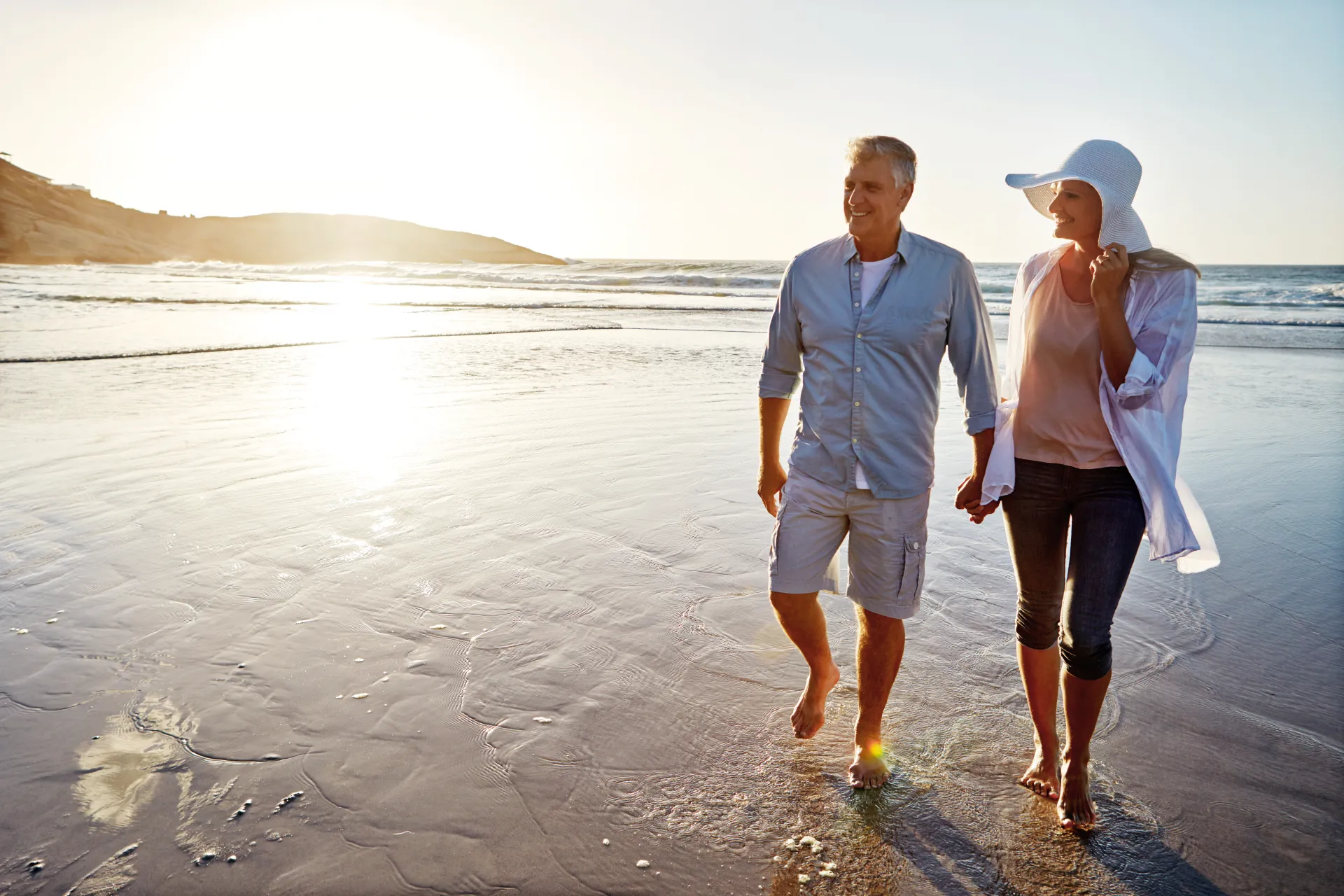 Older couple holding hands walking a long the beach at sunset