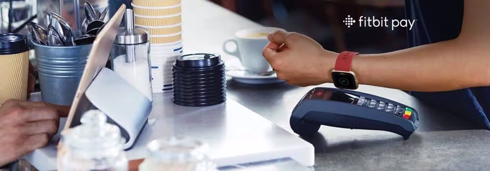 A person wearing a smartwatch putting their arm up to an eftpos machine to pay using Fitbit Pay