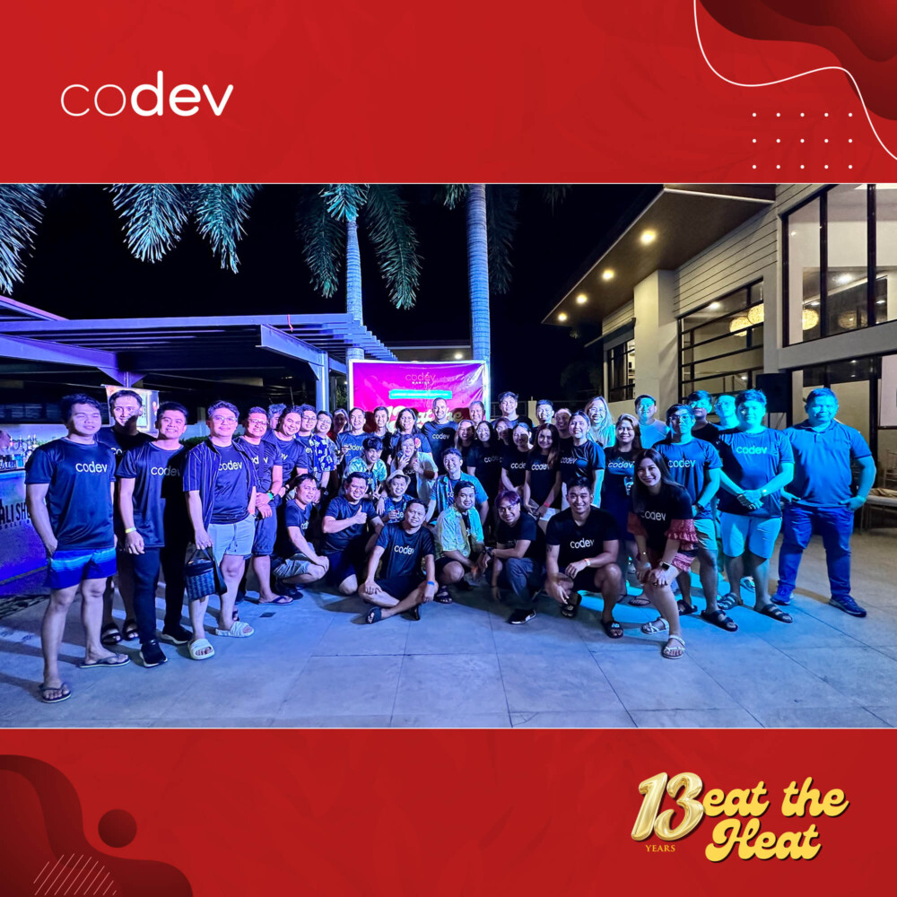 CoDev employees in Manila pose for an anniversary group photo in a garage area at night.