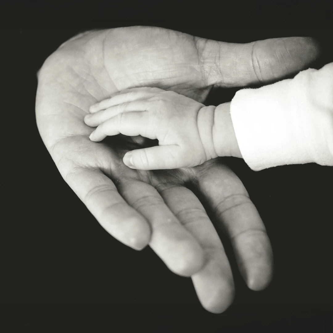 Person wearing a gold ring and bracelets writing in a lined notebook with a red pen, with ripped jeans visible.