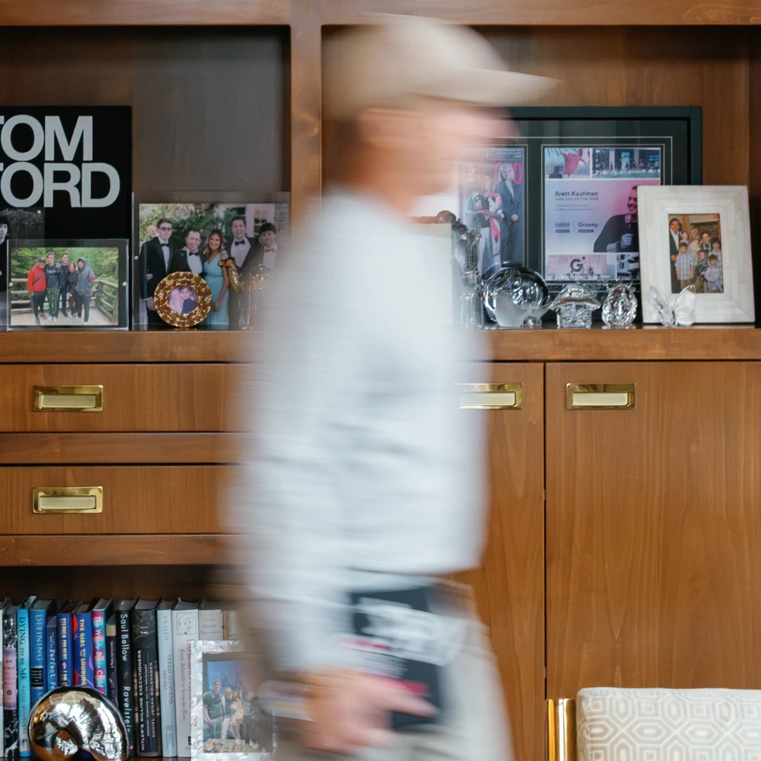 Man in black hoodie and cap holding a coffee cup and tablet, standing in front of a building under construction.