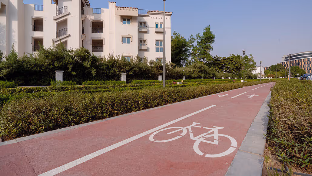Red bicycle lane beside landscaped buildings at Dubai Knowledge Park.