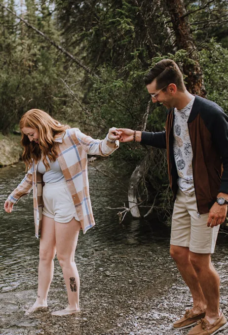 a couple wades into the water. he is helping her to balance