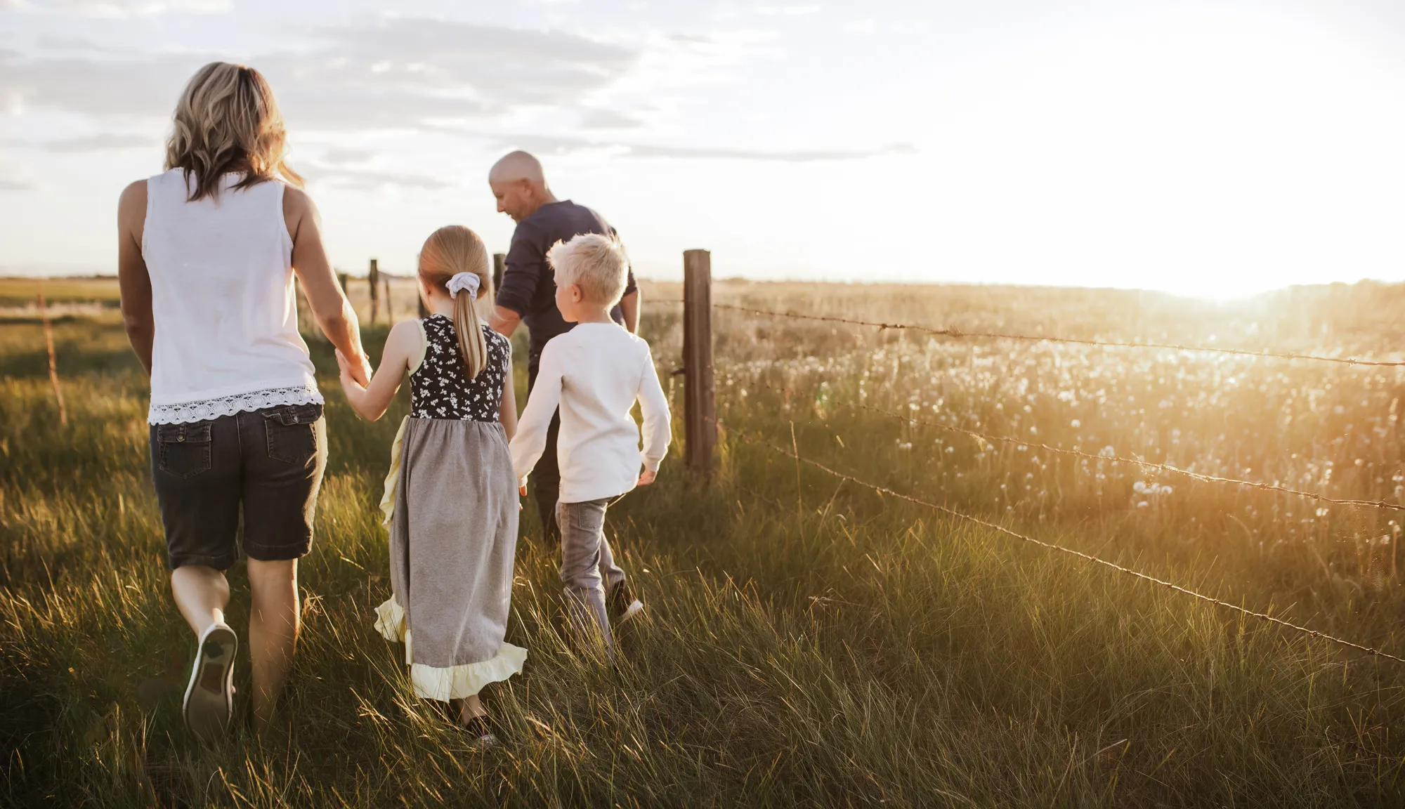 a family walks together through a large field in golden hour