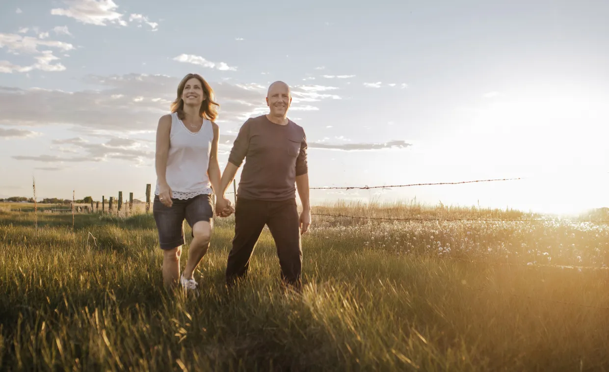 a man and woman walking through a wheat field at golden hour