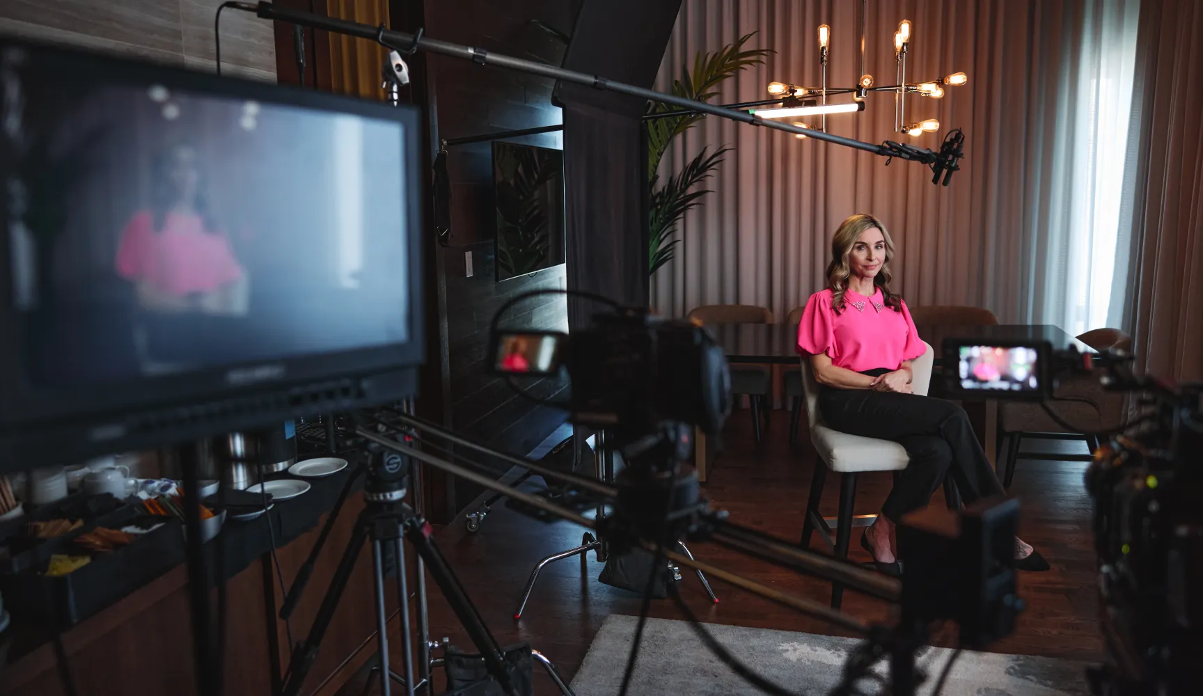 Behind-the-scenes of a professional video shoot, with a woman in a pink blouse seated for an interview, showcasing the agency's video production expertise.