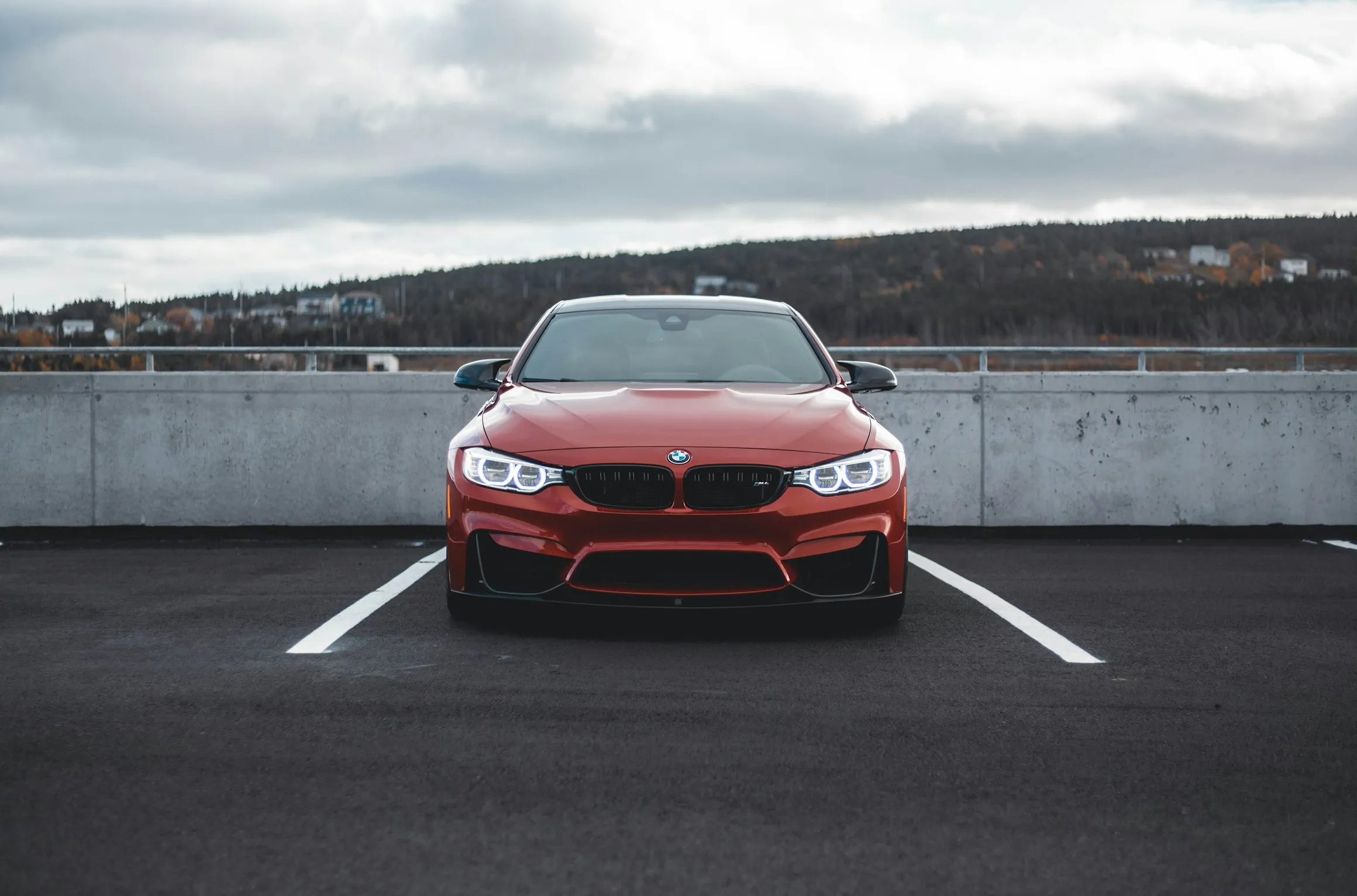 A modern red BMW car is parked in a parking spot on an empty rooftop lot.