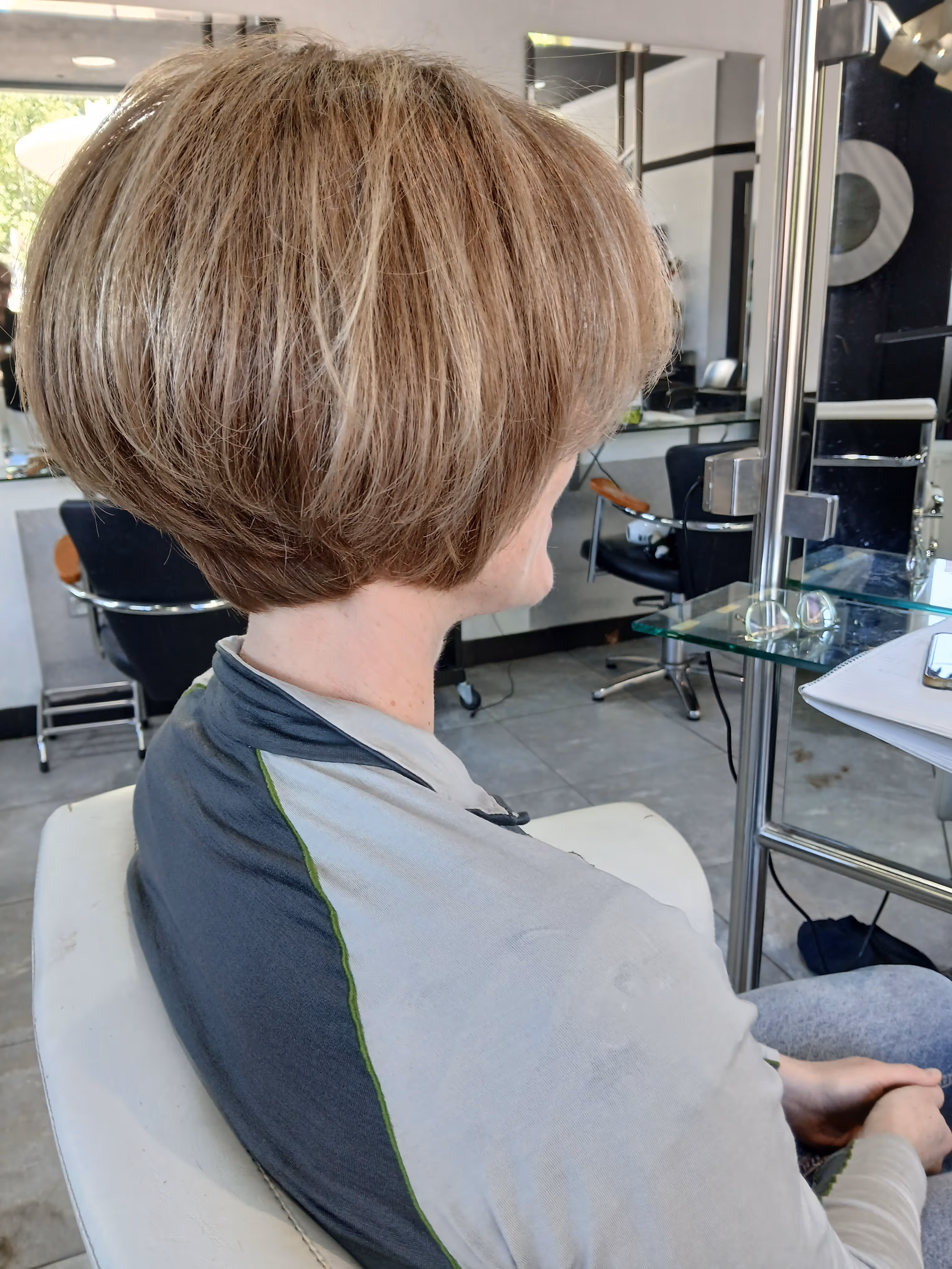 Woman with a short layered bob haircut sitting in a salon chair, facing sideways.