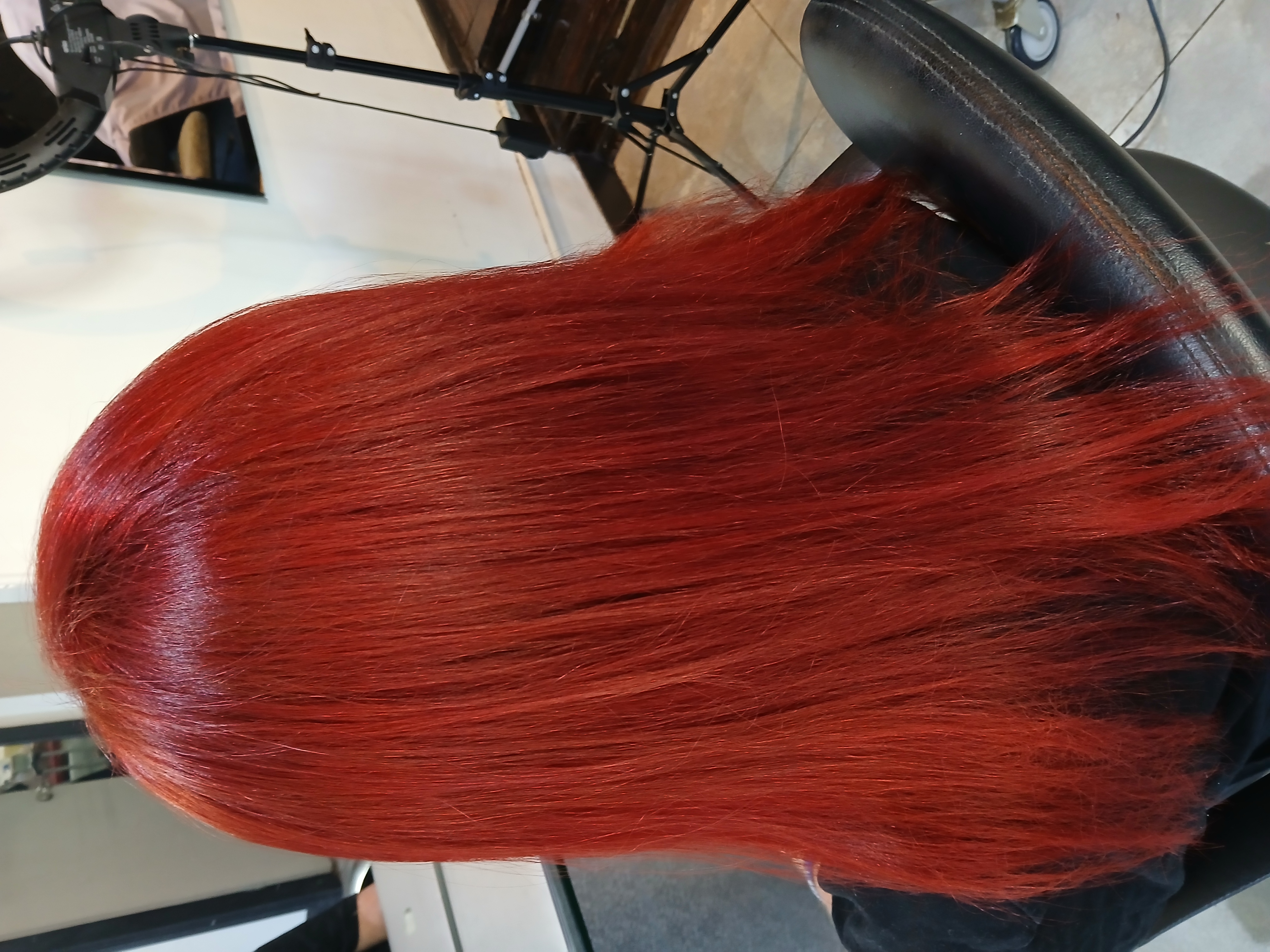 Person seated in salon chair showing vibrant straight red hair from the back.