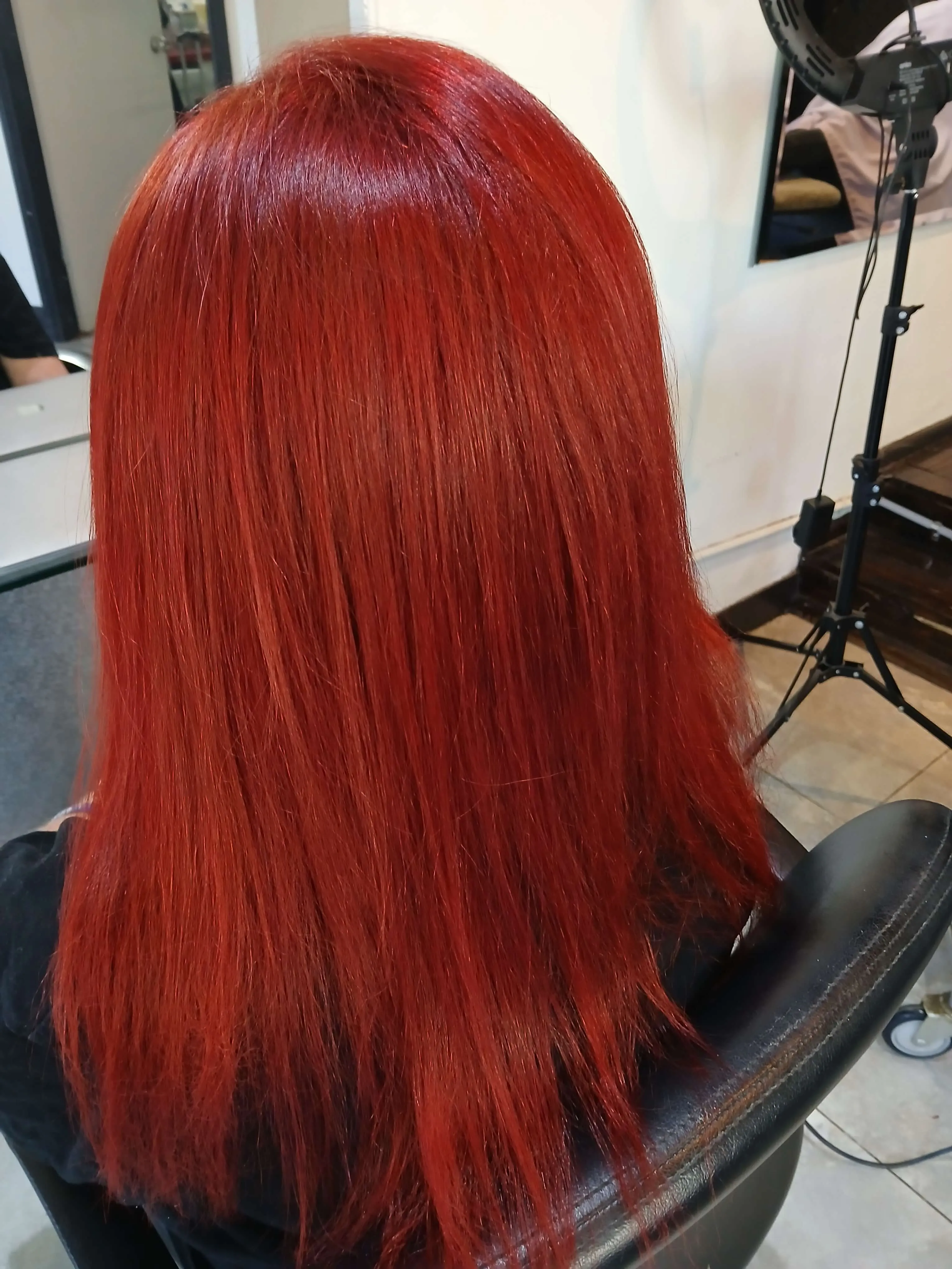 Person with long, straight, vibrant red hair sitting in a salon chair.