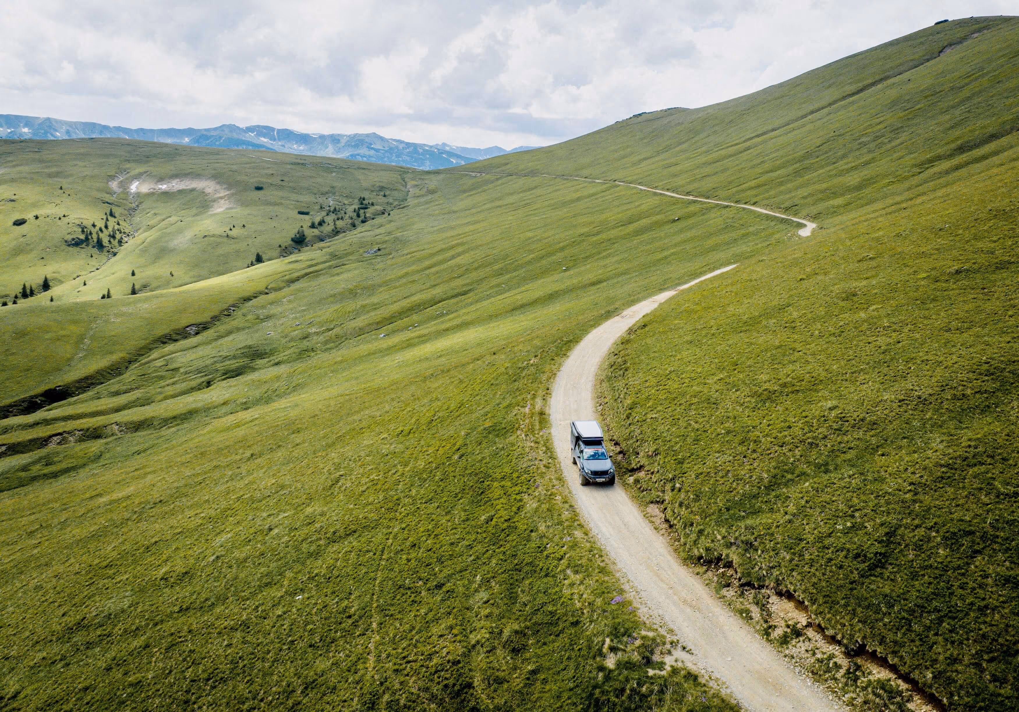 Geländewagen mit aufgestelltem Dach auf schmalem, gewundenem Weg durch grüne Hügellandschaft.