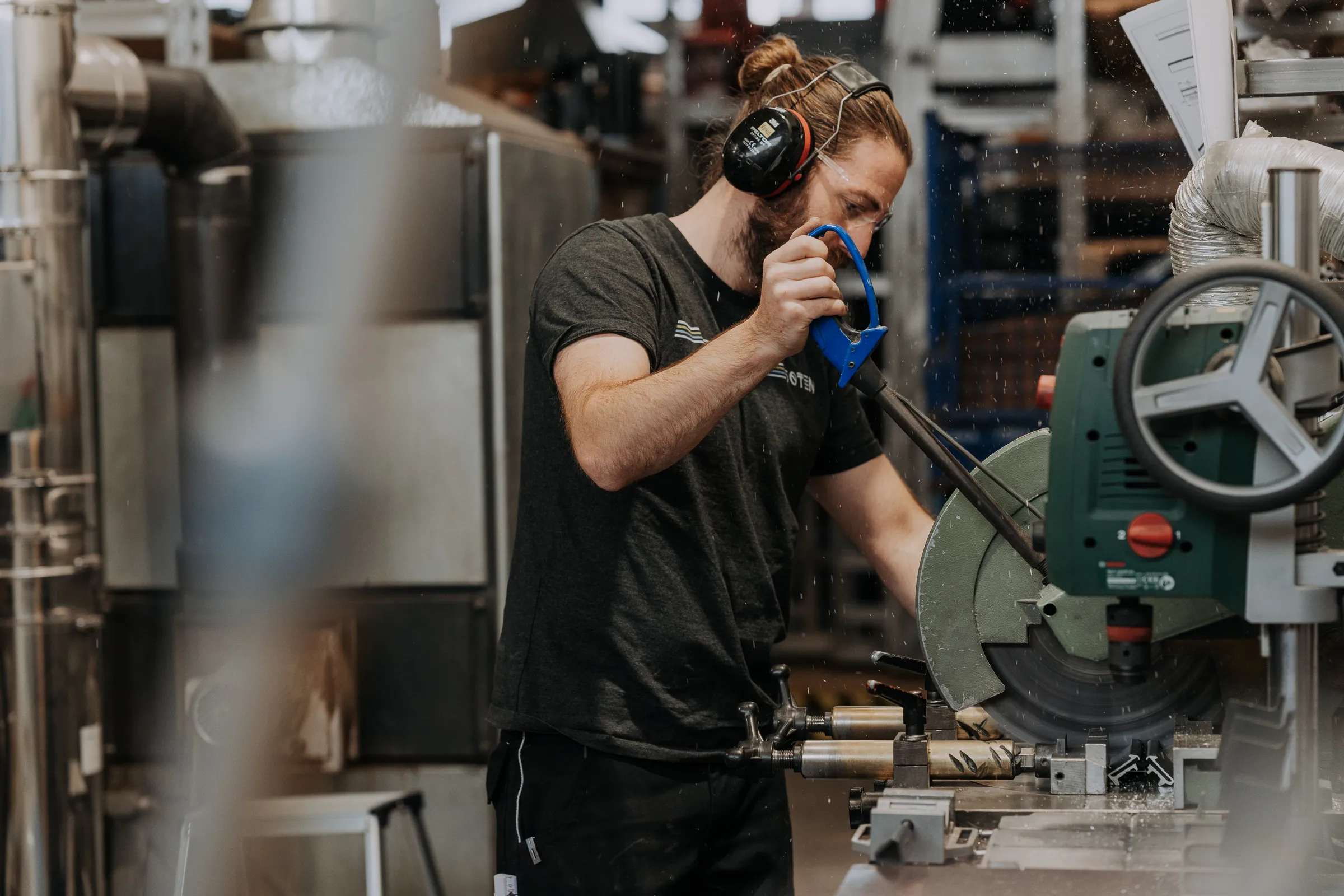 Mann mit Gehörschutz bedient eine Kreissäge in einer Werkstatt.