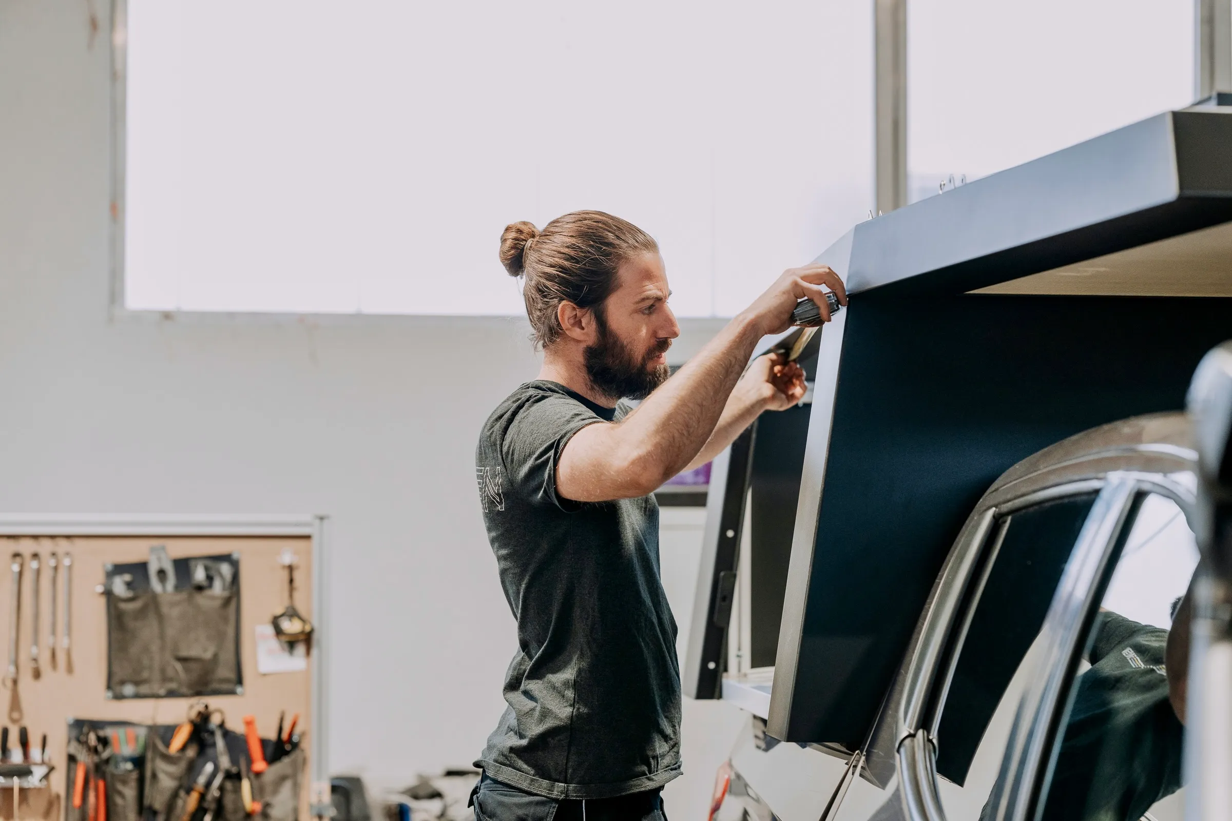 Mann mit Dutt öffnet eine schwarze Pick-up-Kabine in einer Werkstatt.