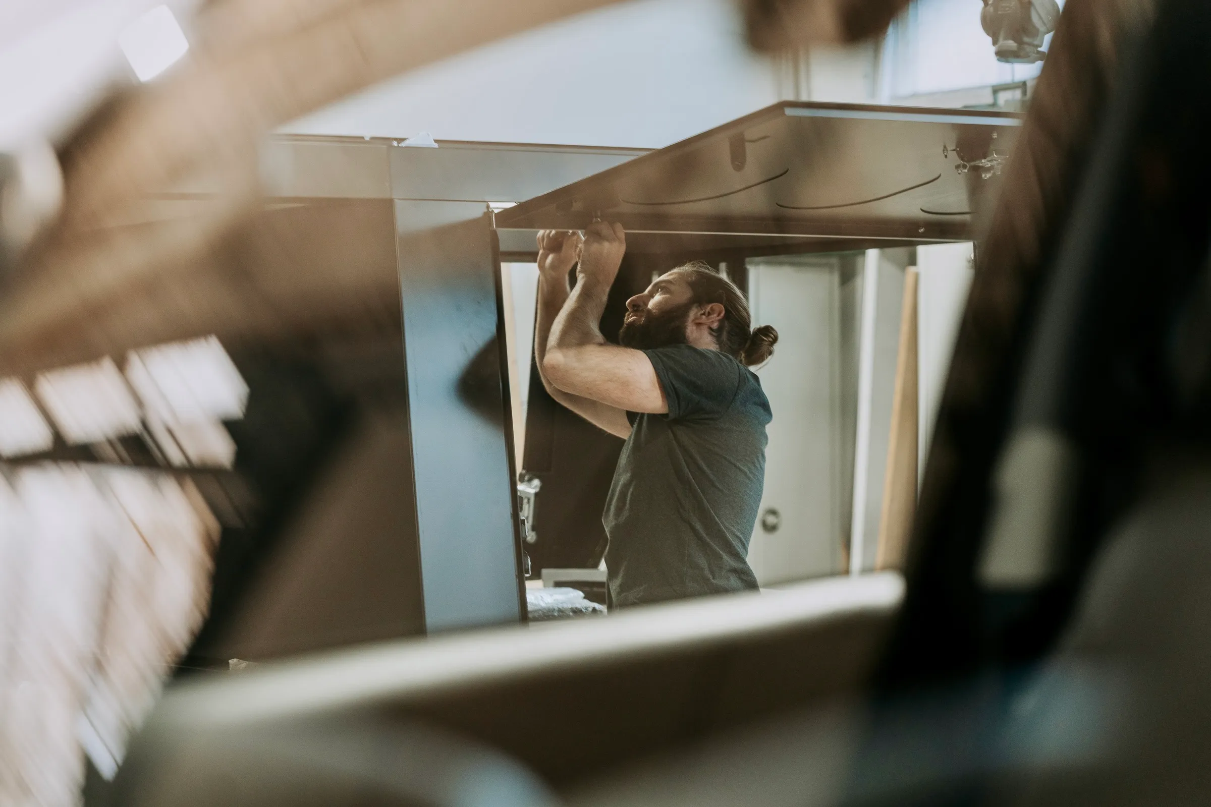 Mann mit Zopf, der an einer hohen Metallstruktur in einer Werkstatt arbeitet.