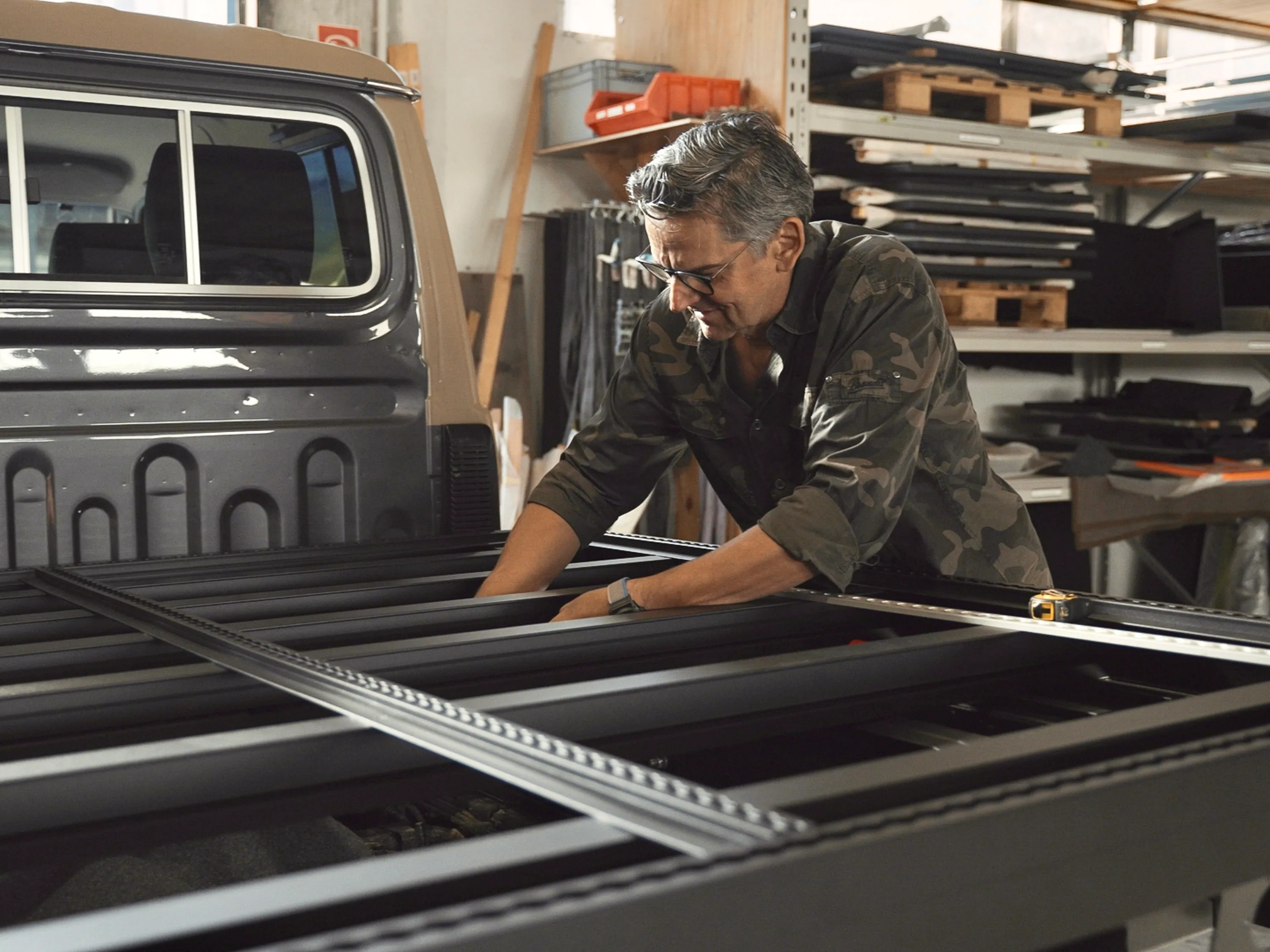 Mann arbeitet an einem schwarzen Metallgestell auf der Ladefläche eines Pick-up in einer Werkstatt.