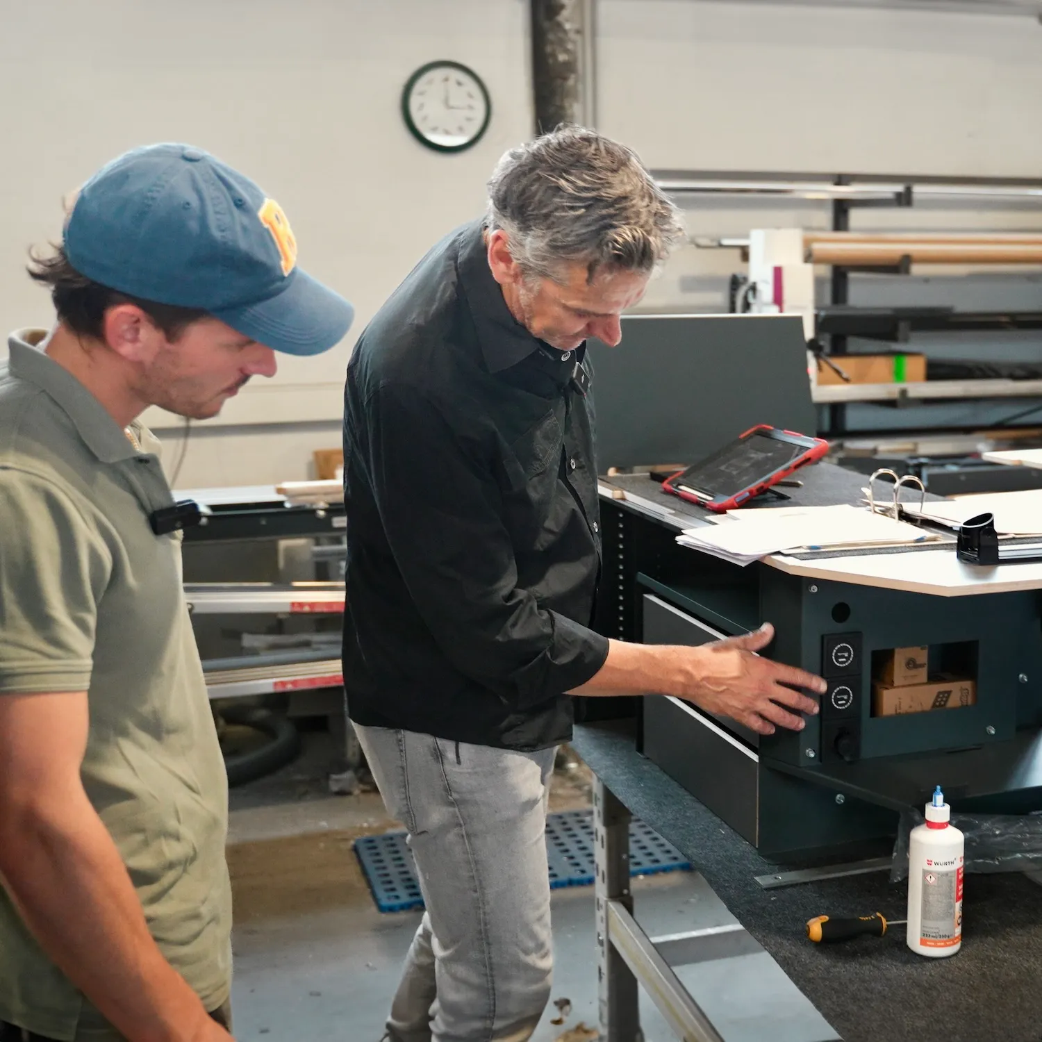 Zwei Männer prüfen ein technisches Gerät auf einem Tisch in einer Werkstatt.