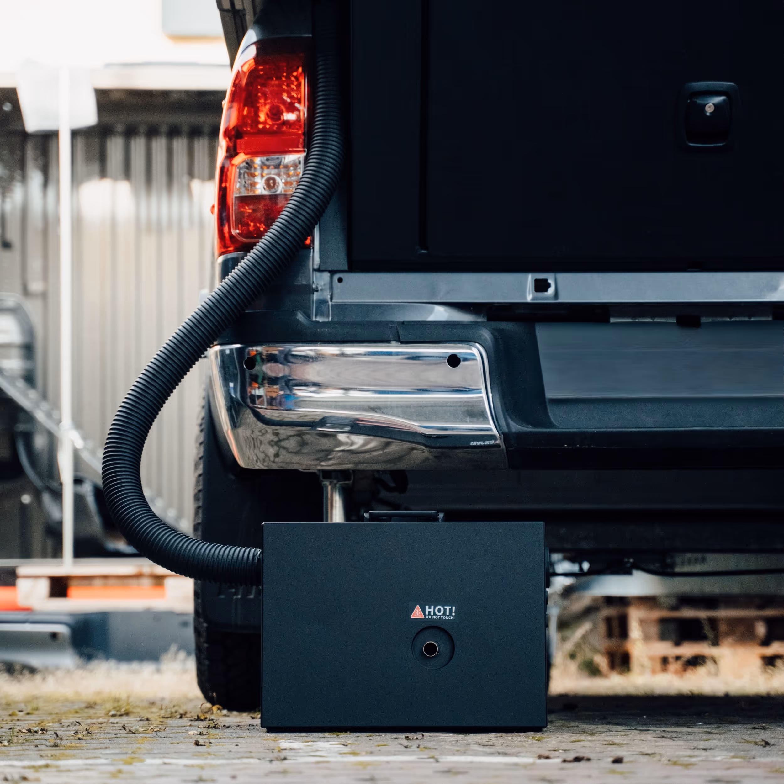 Heizeinheit mit Schlauch, angeschlossen an die Rückseite eines schwarzen Pickup-Truck-Betten-Campers.