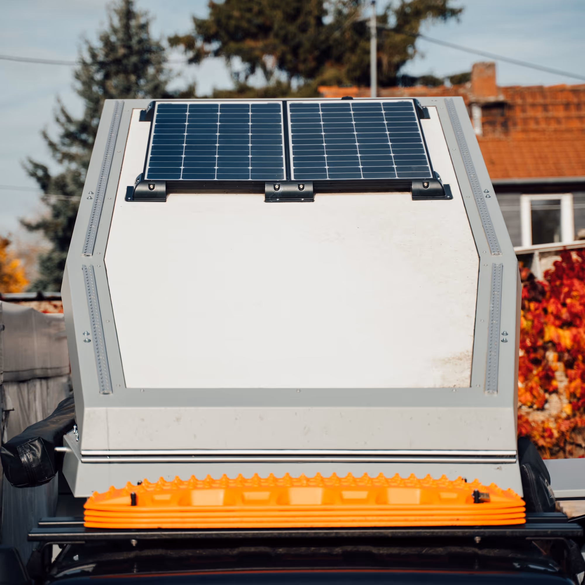 Nahaufnahme eines weißen Wohnwagens mit zwei Solarmodulen auf dem Dach und orangenem Ausrüstungsgegenstand vorne.