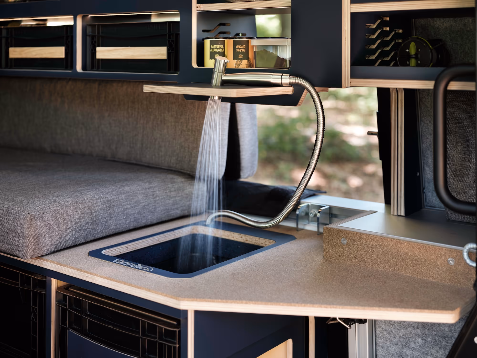 Kompakte Küchenzeile mit abklappbarem Wasserhahn und fließendem Wasser in einem Fahrzeugausbau.