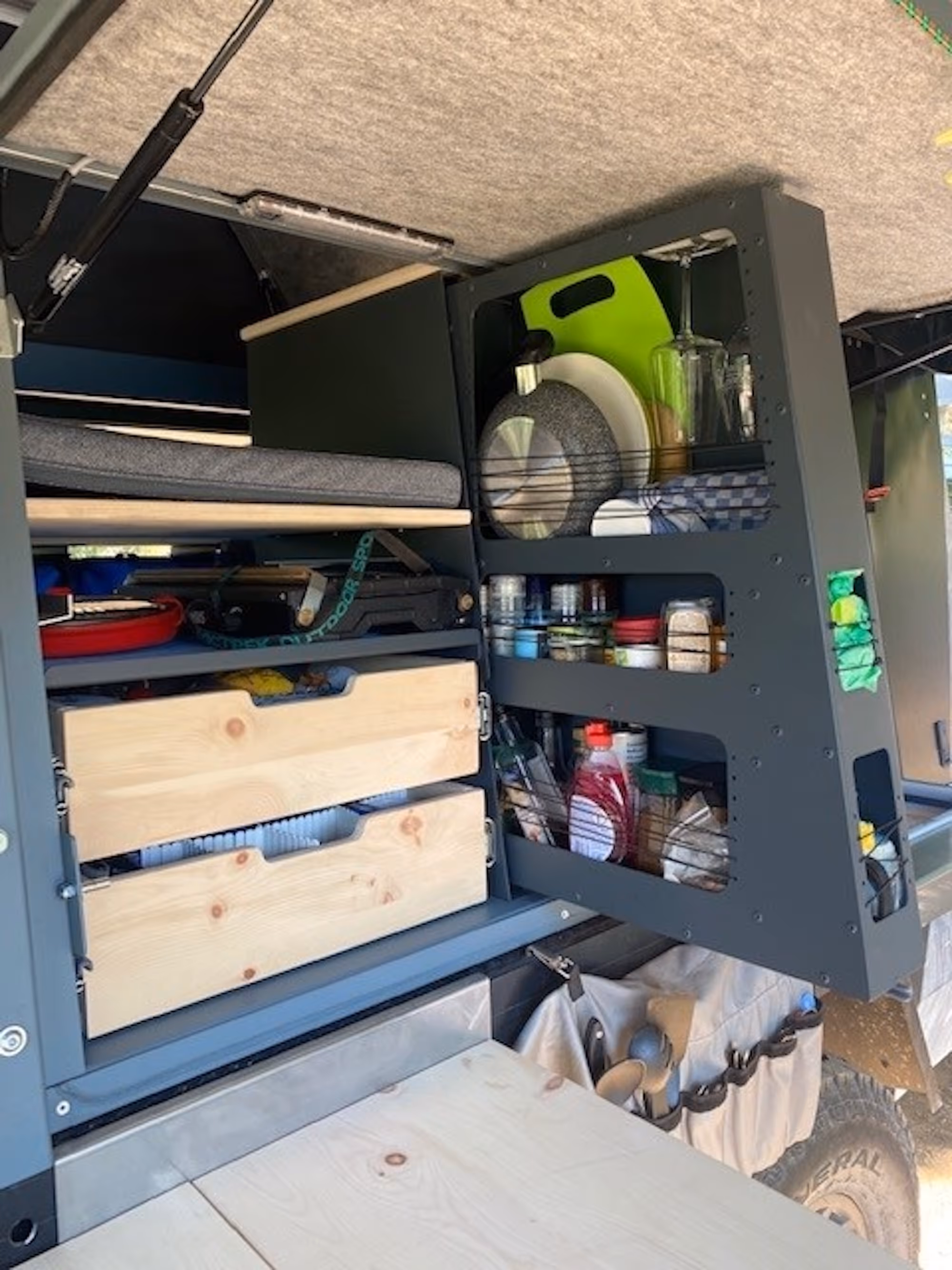 Camping-Küchenschrank mit Geschirr, Besteck, Gewürzen und Kochutensilien in einem Outdoor-Fahrzeug.