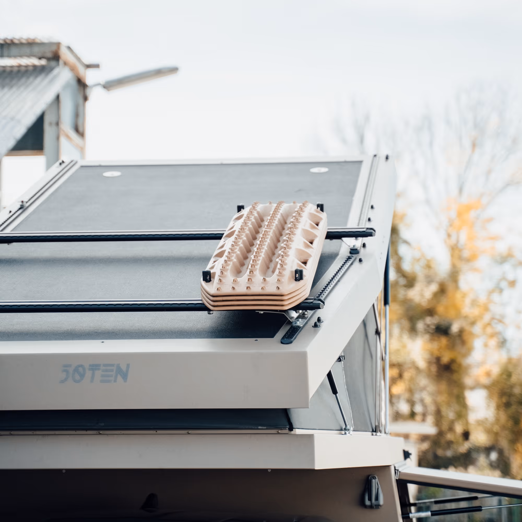 Geländewagen mit montiertem Sandblech auf dem Dachträger vor unscharfem Herbsthintergrund.