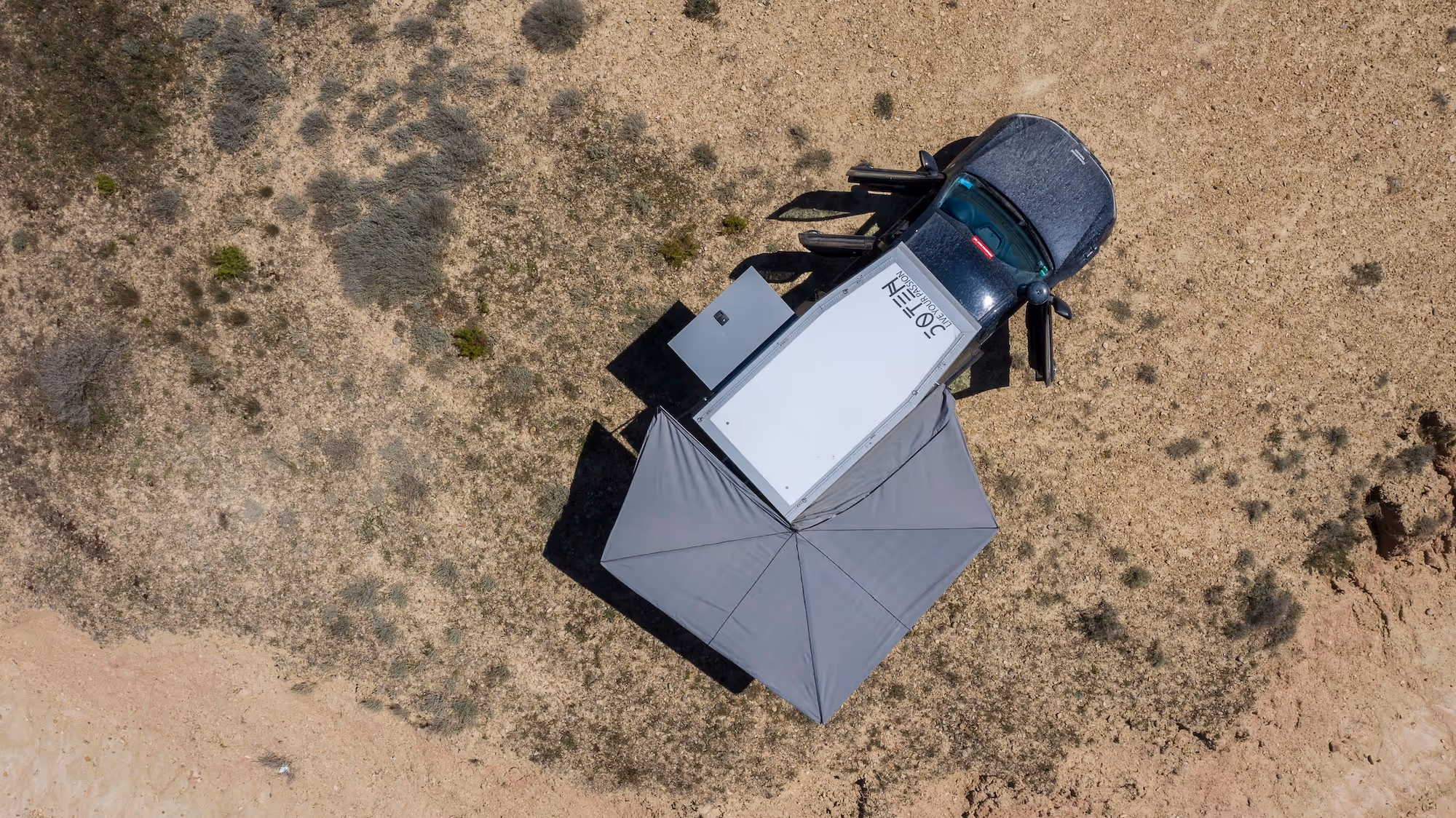 Draufsicht eines Pick-up-Trucks mit aufgeklapptem grauem Sonnenschutz und geöffneter Tür auf einem trockenen, kargen Gelände.